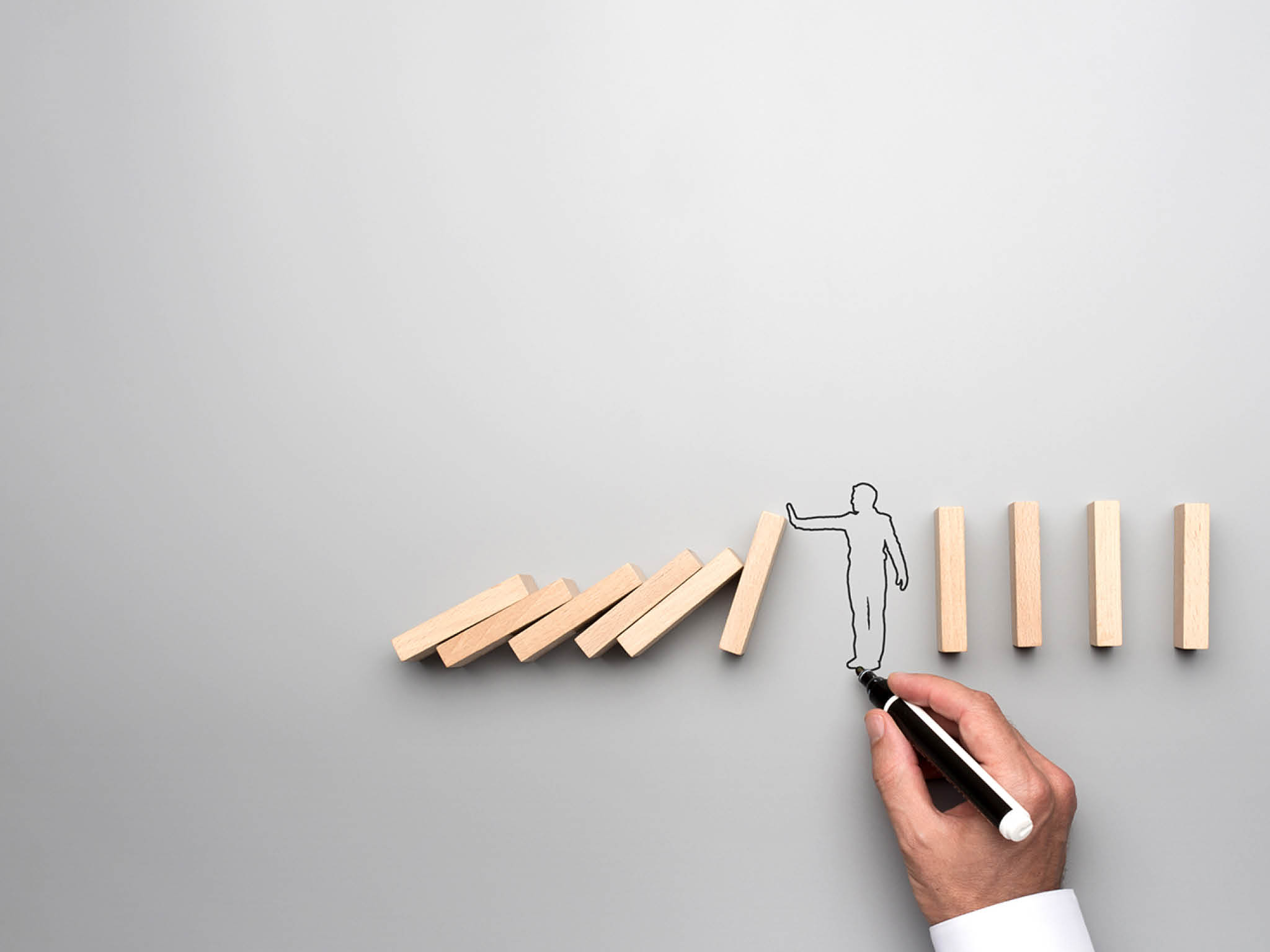 Man drawing the outline of a businessman stopping the domino effect in a conceptual image on gray background.