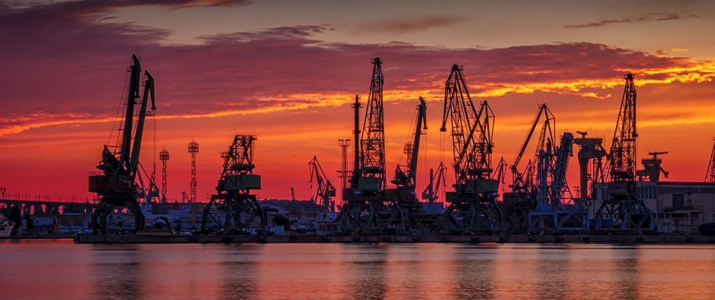 Silhouettes of port cranes at stunning red sunset. Cargo ship terminal at the twilight scene.
