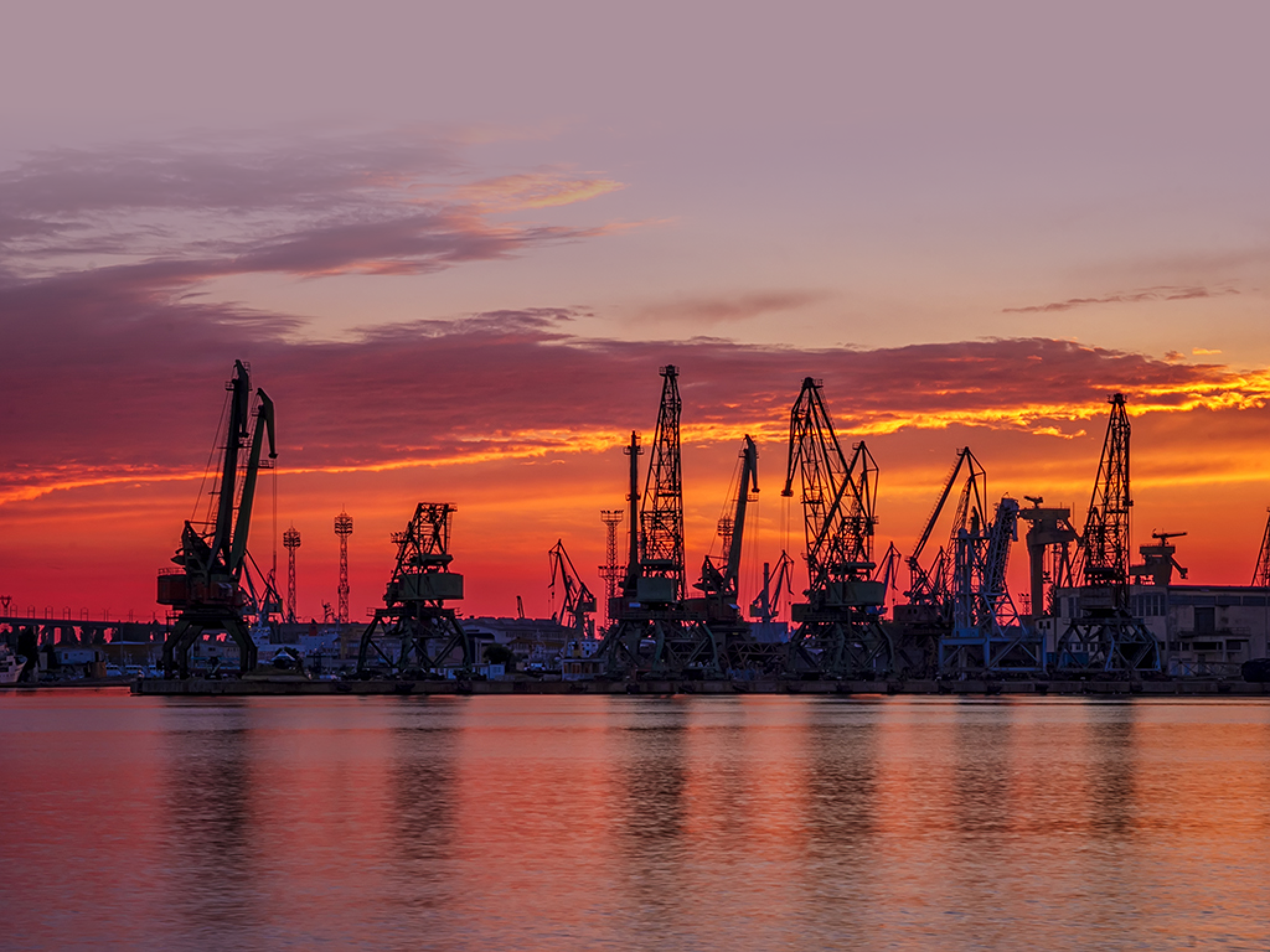 Silhouettes of port cranes at stunning red sunset. Cargo ship terminal at the twilight scene.