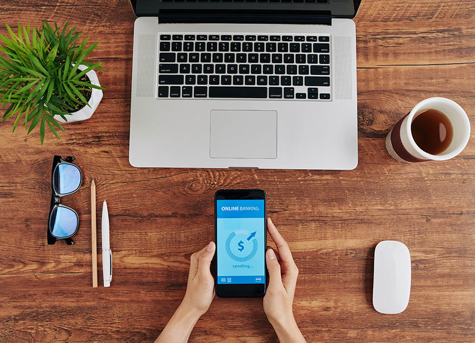 Hands of woman sitting at table with opened latop and cup of tea and paying for service via banking application