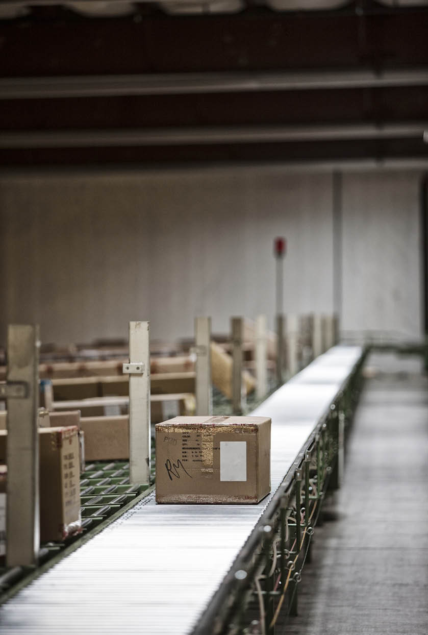 Interior view of a large distriubiton warehouse showing a mototized converyor system to move products stored in cardboard boxes.