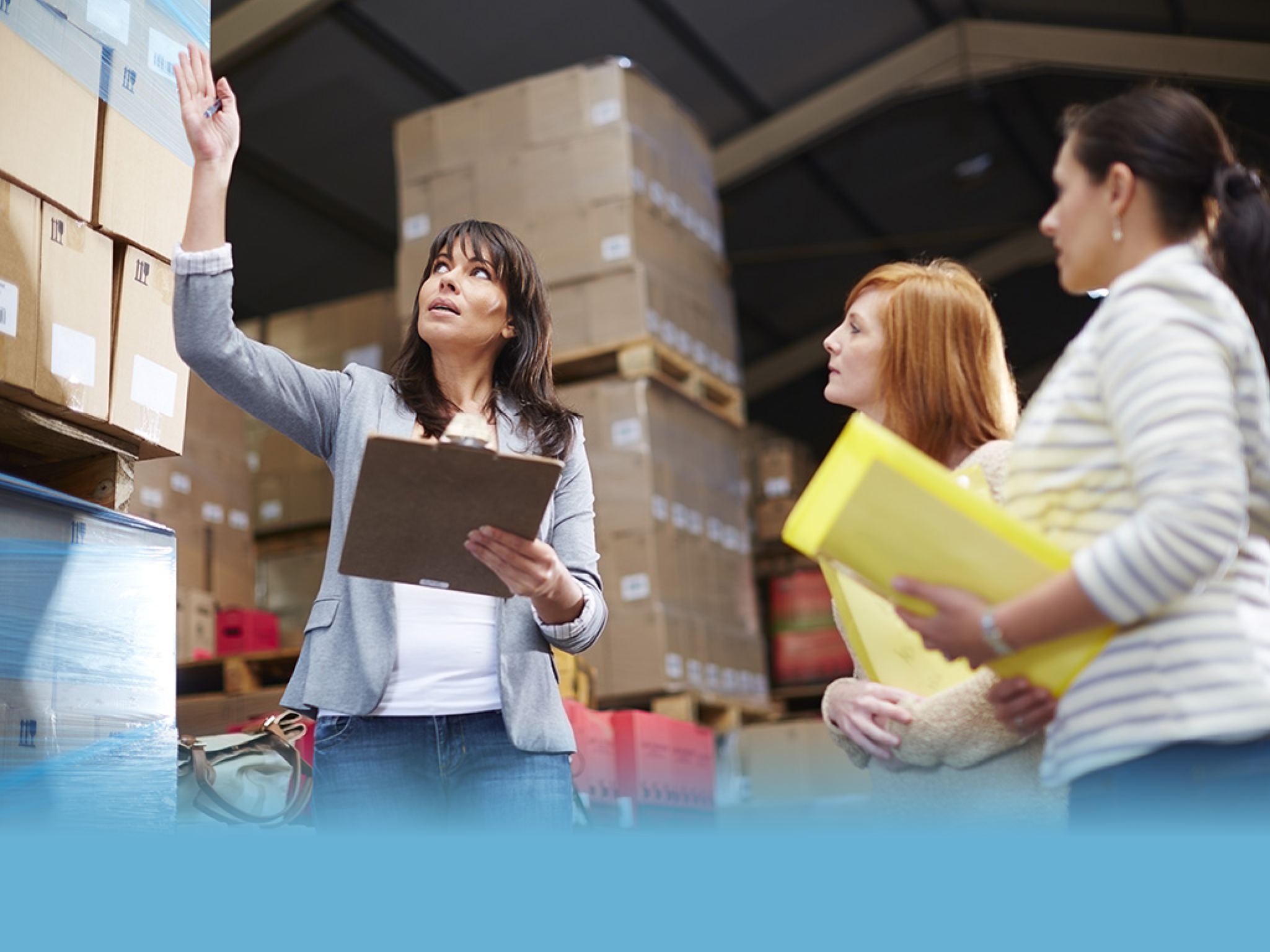 Woman with clipboard in warehouse talking to women